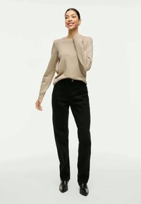 Camisola de malha bege com mangas longas, combinada com calças pretas de perna reta. O calçado são botins pretos de bico redondo. Estilo minimalista.