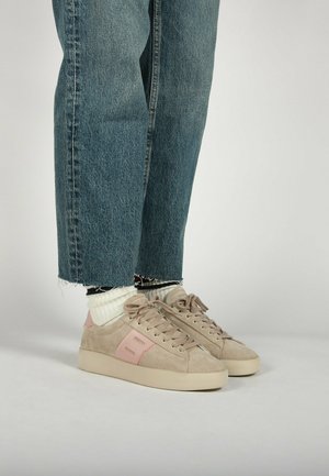 Beige suede sneakers met roze accenten, ronde neus, platte zool en vetersluiting. Gepaard met opgerolde denim jeans en crèmekleurige sokken.