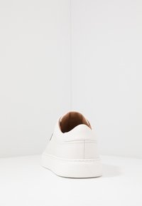 White leather sneaker with a rounded toe, smooth texture, and a low top. Features a contrasting beige interior and minimalistic design.