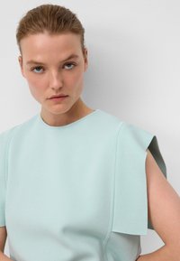 Jasnoniebieska bluzka o teksturowym wykończeniu, z krótkimi rękawami o przedłużonym fasonie, okrągłym dekoltem i dopasowanym kroju.