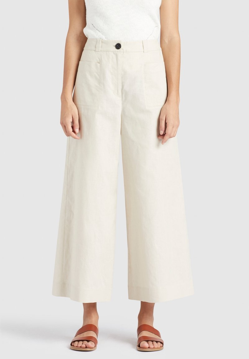 Beige wijde pantalon van lichtgewicht stof, met een hoge taille, twee voorkanten zakken en een zwarte knoopsluiting.