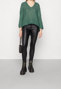 Grön stickad tröja med V-ringning, kombinerad med svarta läderleggings och kraftiga svarta snörstövlar. Har en avslappnad passform och texturerad tyg.