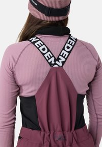 Bordeaux- og sort højhalset beklædningsgenstand med ribbet struktur, der har et krydsryg-design og mærkede stropper. Stoffet ser let og strækbart ud.
