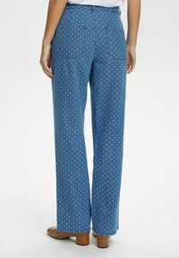 Mėlyni džinsai su taškeliais, aukštu liemeniu, tiesiomis kojomis ir dviem galinėmis kišenėmis. Baigti su švariu apvadu ir be dekoratyvinių elementų.