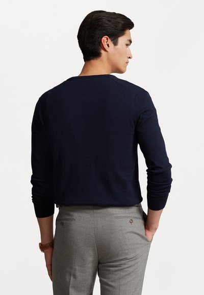Marineblauwe longsleeve trui met ronde hals, gemaakt van soepel materiaal. Grijze op maat gemaakte broek met zakken en subtiele details aan de achterkant.