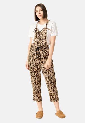 Pantalones de mezclilla con estampado de leopardo sobre una base color beige claro, tirantes ajustables y cintura con cordón, combinados con una camiseta blanca y zuecos beige.