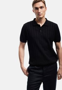 Schwarzes Strick-Polohemd mit gerippter Textur, Knopfleiste mit drei Knöpfen und kurzen Ärmeln, kombiniert mit dunklen Hosen. Einfaches und modernes Design.
