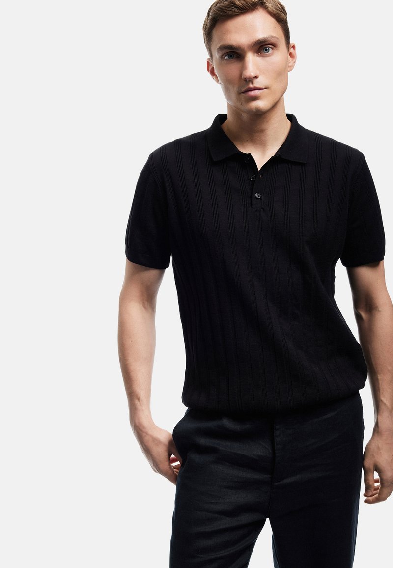 Schwarzes Strick-Polohemd mit gerippter Textur, Knopfleiste mit drei Knöpfen und kurzen Ärmeln, kombiniert mit dunklen Hosen. Einfaches und modernes Design.