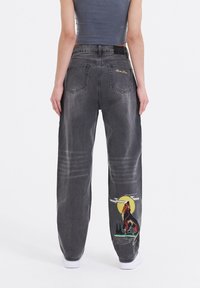 Baggy, falmede sorte jeans med et ulv grafik og teksten "Born to Be Wild", med dobbelte baglommer og et tekstureret stof.