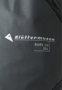 Schwarzer Textilrucksack mit dem Markenlogo "Klättermusen" und dem weißen Text "BURE 2.0 20L". Das Material hat eine strukturierte Oberfläche mit subtilen Mustern.