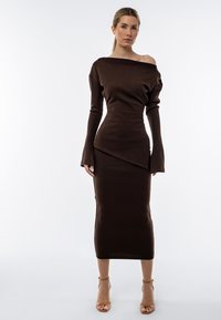 Abito a coste marrone con scollatura off-shoulder e maniche lunghe. Silhouette aderente con dettaglio dell'orlo asimmetrico e tessuto testurizzato.