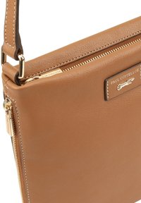 Kastanjebruine leren schoudertas met gouden rits en metalen logo plaat met de tekst "Paul Costelloe" aan de voorkant.