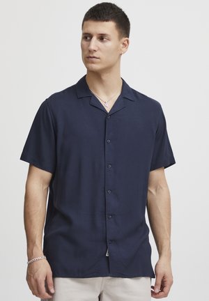Camisa azul marino de manga corta, con botones y hecha de una tela suave. Presenta un cuello tipo camp y un corte relajado con un ligero brillo.