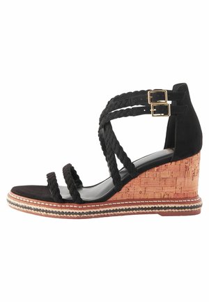 Svart mocka kilklack sandal med flätade remmar, korkkilklack och dekorativ söm längs sulan. Öppen tå-design.