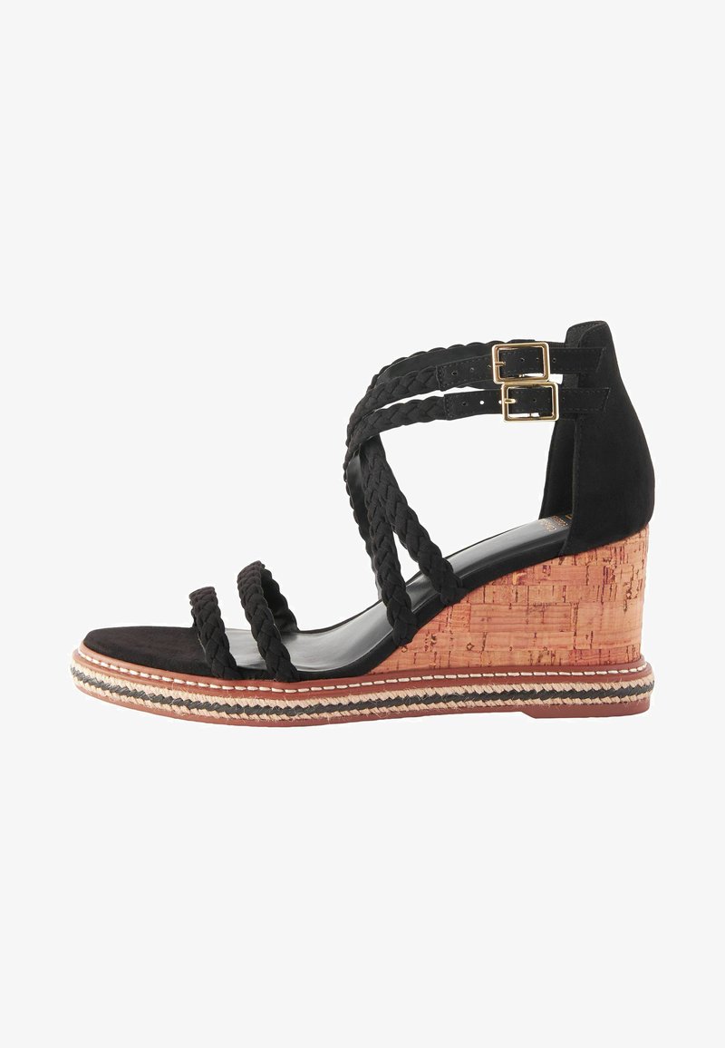 Sandale à talon compensé en suède noir avec des straps tressés, talon en liège et surpiqûres décoratives le long de la semelle. Design à bout ouvert.