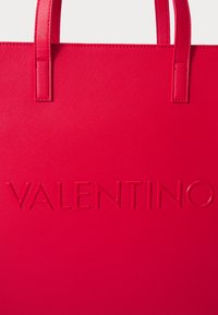 Κόκκινη υφασμάτινη τσάντα tote με ανάγλυφο λογότυπο "VALENTINO", διπλές λαβές στην κορυφή και κομψό, μινιμαλιστικό σχέδιο.