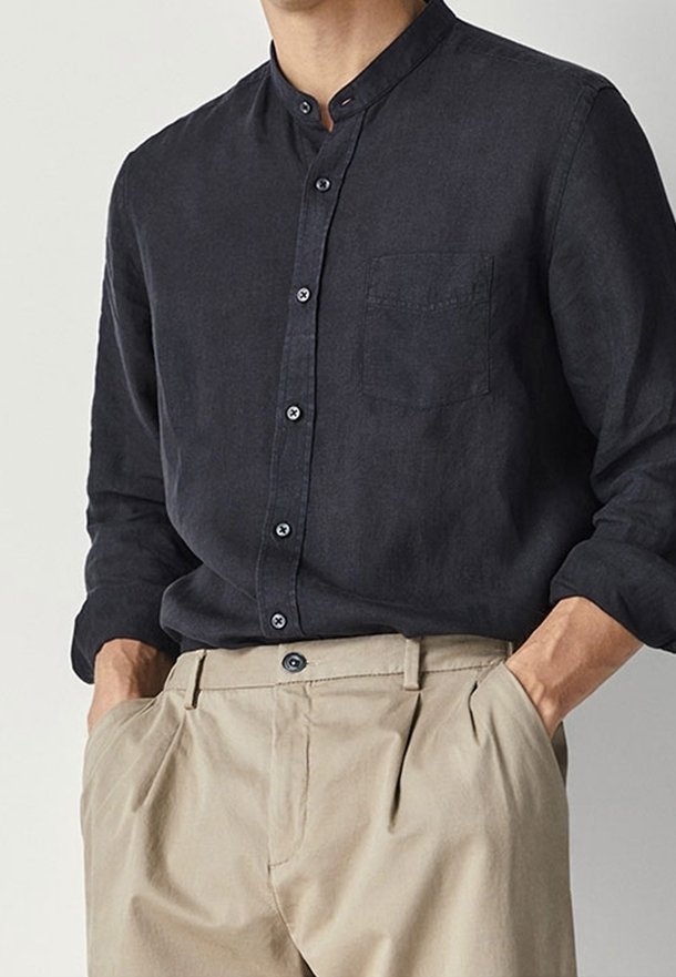 Chemise en lin gris foncé avec col Mao, manches longues et une poche poitrine. Dotée d'un devant boutonné avec des boutons contrastants.