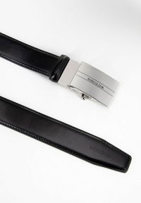 Cinturón de cuero negro con una hebilla de plata pulida con la inscripción "WITTCHEN". La hebilla presenta un diseño rectangular elegante con líneas limpias.