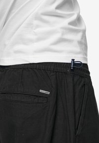 Svarta shorts med elastiskt midjeband, tillverkade av mjukt tyg, med en sidoficka, märkesetikett och dragsko vid midjan.