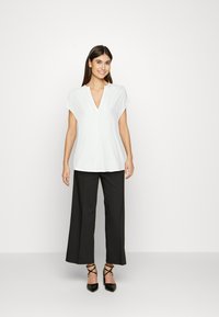 Weißes kurzärmeliges Bluse mit V-Ausschnitt, kombiniert mit schwarzen weiten Hosen und schwarzen spitzen Absatzschuhen. Einfacher, glatter Stoff und klare Linien.