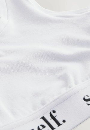 Zatvoren kadar bijelog tekstilnog odjevnog predmeta s djelomično vidljivim crnim tekstom na rubu ili pojasu.