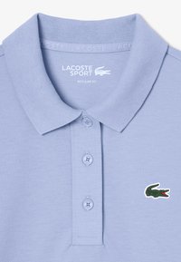 Polo shirt azzurro chiaro in tessuto strutturato, con un bottone a tre e un logo di coccodrillo verde sul lato sinistro del petto.