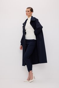 Marineblå lang frakke, hvid ribbet sweater med sidelukninger, marineblå tapered bukser og hvide spidse hæle på en minimalistisk baggrund.