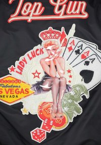 Svart tyg med broderade lappar: en pin-up flicka, spelkort och tärningar, med färgglad text och intrikata detaljer som framkallar ett vintage Vegas-tema.