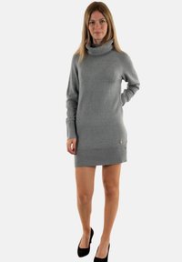 Abito grigio lavorato a maglia con colletto alto, polsini e orlo a coste. Presenta una leggera luminescenza e un piccolo logo decorativo nella parte inferiore.