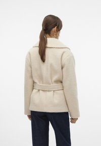 Beige ullblandad kappa med klassisk krage, bälte vid midjan och strukturerad yta. Figursydd siluett med sidofickor och lång ärm.
