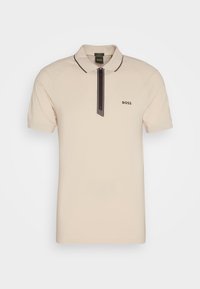 Polo à manches courtes en mélange de coton beige clair, avec un détail zippé noir et un col, et un logo discret sur la poitrine.