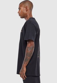 Sort T-shirt med kortærmer og rund hals; har et grafisk print på ryggen; lavet af blødt, åndbart bomuldsstof.