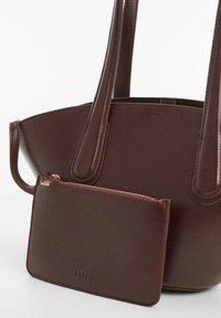 Brun læder tote taske med to håndtag og en lynlåspung. Glat tekstur, minimalistisk design med guldfarvet hardware-akcent.