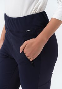 Námořnické elastické kalhoty s boční kapsou na zip, vyrobené z pružného materiálu. Hladká textura a přiléhavý střih, vhodné pro aktivní nošení.