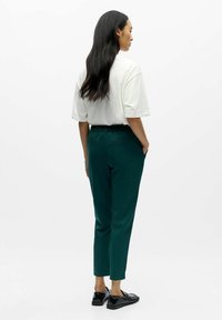 Green tapered pants with an elastic waistband, paired with a loose white t-shirt. Black shoes with a smooth texture and minimal design.