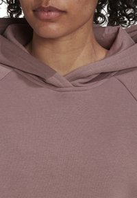 Jasnofioletowa bluza z kapturem, wykonana z miękkiego materiału, z tkaniną o plecionej strukturze oraz podwójnym kapturem, luźnym dekoltem i rękawami raglanowymi.