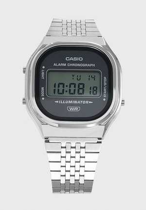 Montre digitale Casio avec bracelet métallique argenté, affichant l’heure 10:08:18, date mardi 14, et dotée d’une alarme, d’un chronographe et d’un illuminateur.