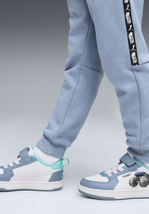 Witte en lichtblauwe sneakers met een klittenbandsluiting, voorzien van een grafisch ontwerp aan de zijkant. Gekleed met lichtblauwe joggingsbroek.