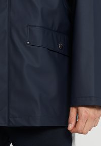 Navy waterproof jacket with a smooth texture, featuring a snap pocket, minimal stitching, and a simple design, showcasing clean lines.