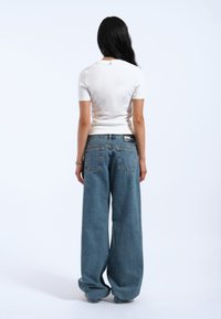 Hvid kortærmet tætsiddende top parret med højtaljede, vide lyseblå denimjeans med baglommer og et sort mærke på taljen.