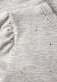 Top grigio chiaro realizzato in un tessuto morbido con scollatura rotonda e dettagli di maniche arricciate. Piccole borchie lucide abbelliscono il davanti.