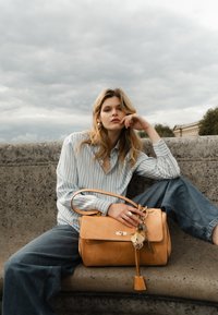 Brun lædertaske med en struktureret design, sølvhardware og en dekorativ nøglering. Tasken har en enkelt skulderrem og en lås.