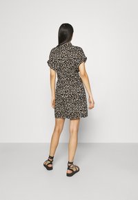 Sukienka w panterkę z krótkimi rękawami, talią ściśniętą, sięgająca powyżej kolan. Posiada kołnierzyk i podwinięte rękawy. Czarne sandały na cienkich paskach.