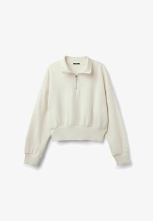 Jasno beżowy, krótki sweatshirt z zamkiem błyskawicznym przy stójce, luźnymi rękawami oraz ściągaczem na dole i przy rękawach. Miękka, gładka faktura.