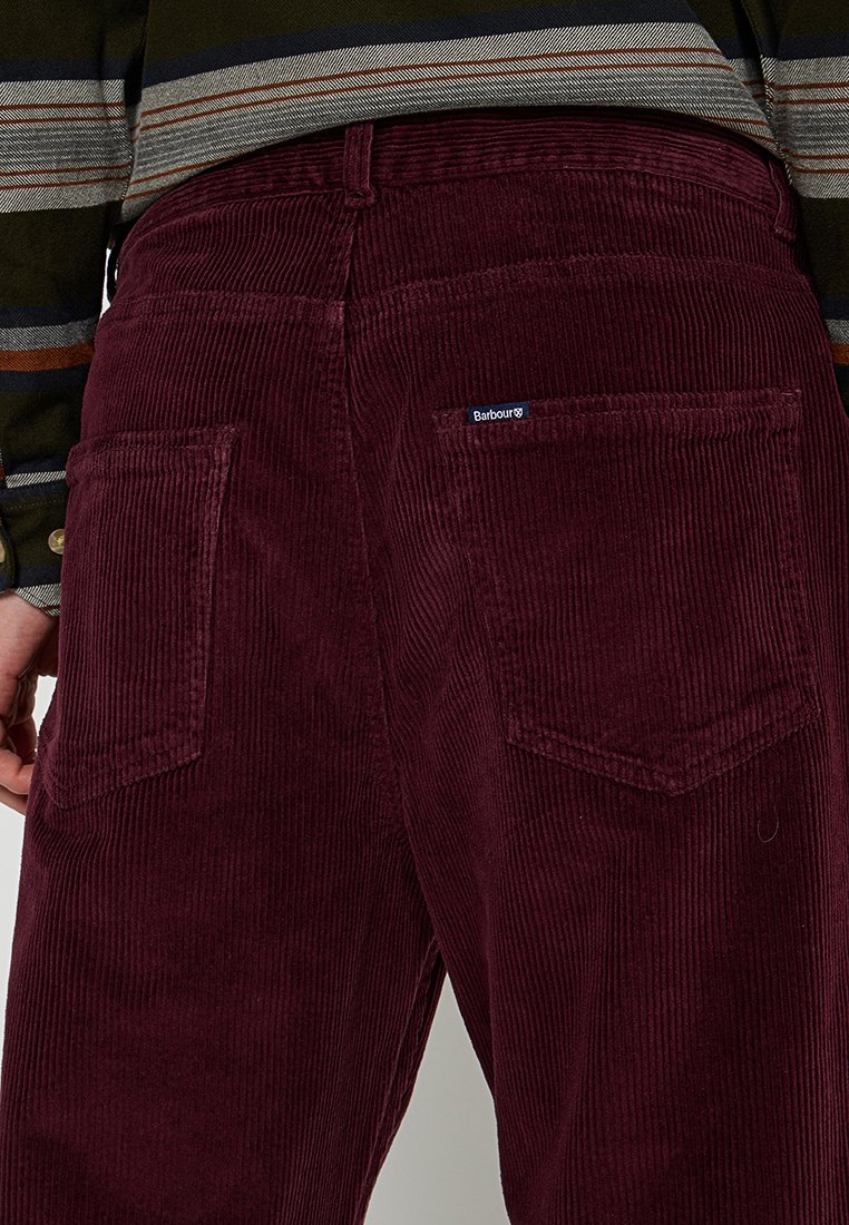 Burgundowe spodnie corduroy z pionowym prążkowaniem, z dwiema tylnymi kieszeniami oraz małym logo Barbour na prawej kieszeni.
