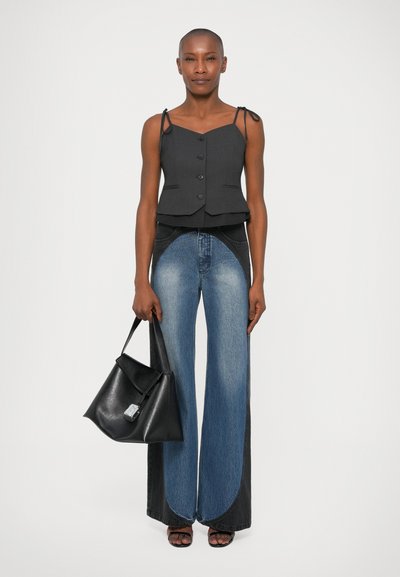 Top peplum nero con bottoni e spalline sottili, abbinato a jeans in denim a gamba larga con pannelli neri e blu a contrasto. Borsa nera.