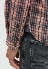 Langarm-Hemd aus Karostoff in Koralle und Marineblau, mit Knöpfen an den Manschetten und einem abgerundeten Saum, kombiniert mit dunkelgrauen Jeans. Strukturiertes Material.