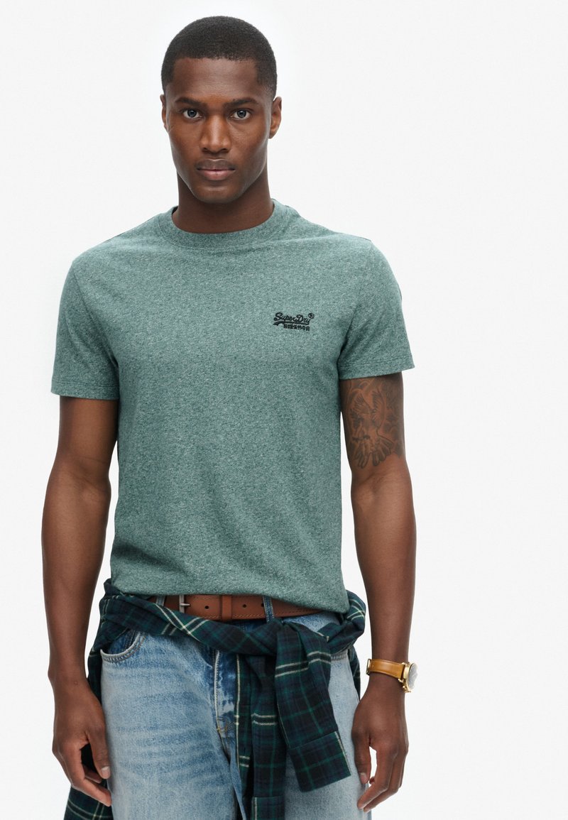 Groene heathered t-shirt met korte mouwen en ronde hals, met een klein zwart logo op de linkerborst. Draag het met blauwe jeans en een geruit overhemd om de taille geknoopt.