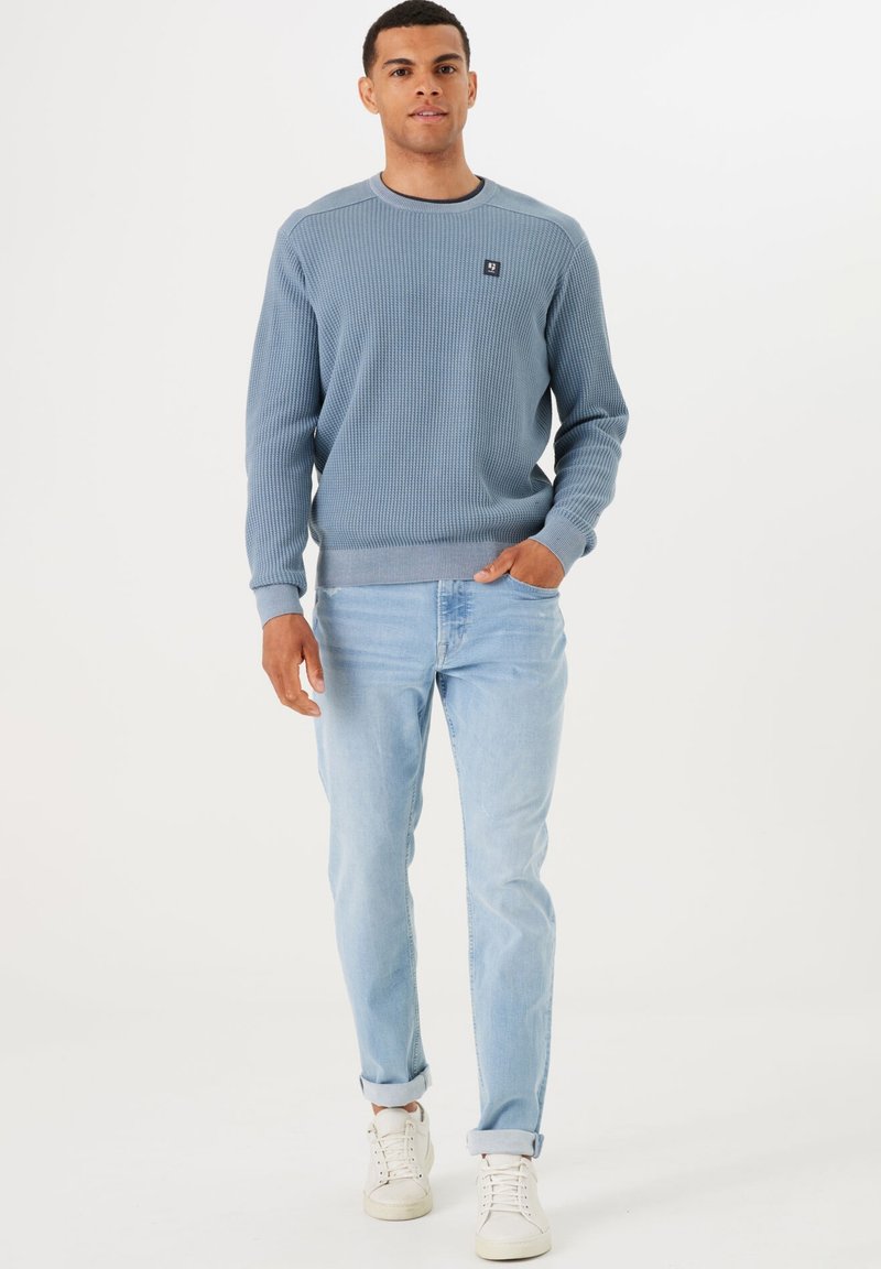 Lichtblauwe wafelgebreide trui met een ronde halslijn, geribde manchetten en zoom. Draagt bij lichte blauwe jeans en witte sneakers.