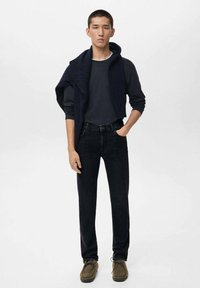 Suéter navy sobre los hombros, camiseta de manga larga gris, jeans oscuros y zapatos de ante marrón; texturas suaves y paleta de colores neutros.